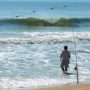 A man wades into the water surf fishing